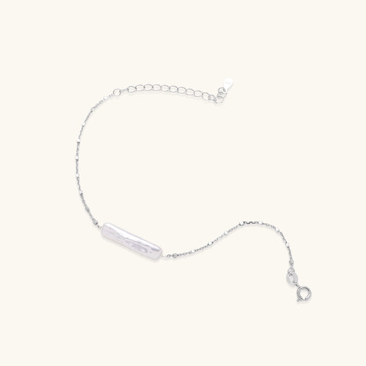 Delicate sterling silver chain bracelet with an organic white baroque pearl centerpiece on neutral background