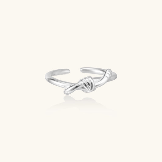 Delicate sterling silver ring with geometric knot design on white background, showcasing adjustable open band.