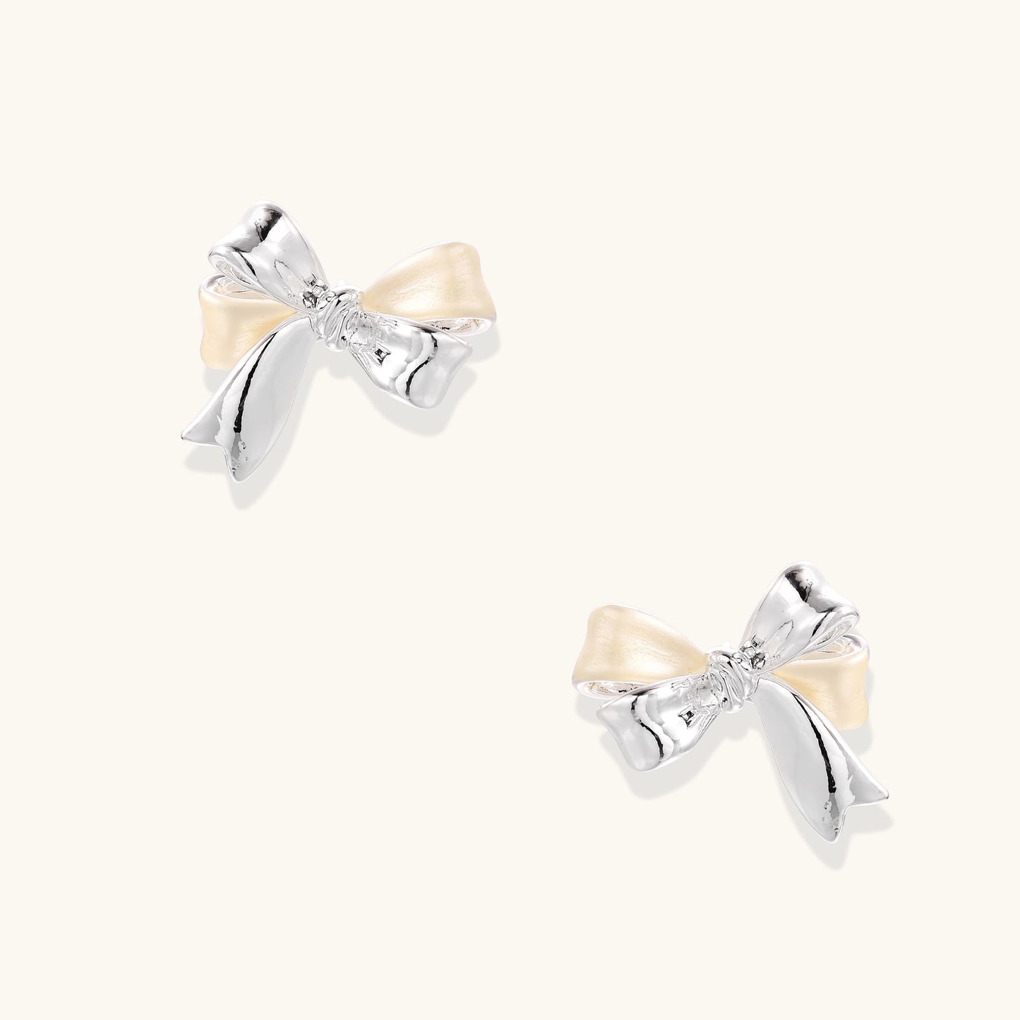 Close-up of bow-shaped stud earrings with 18K gold plated brass and silver details on white background.
