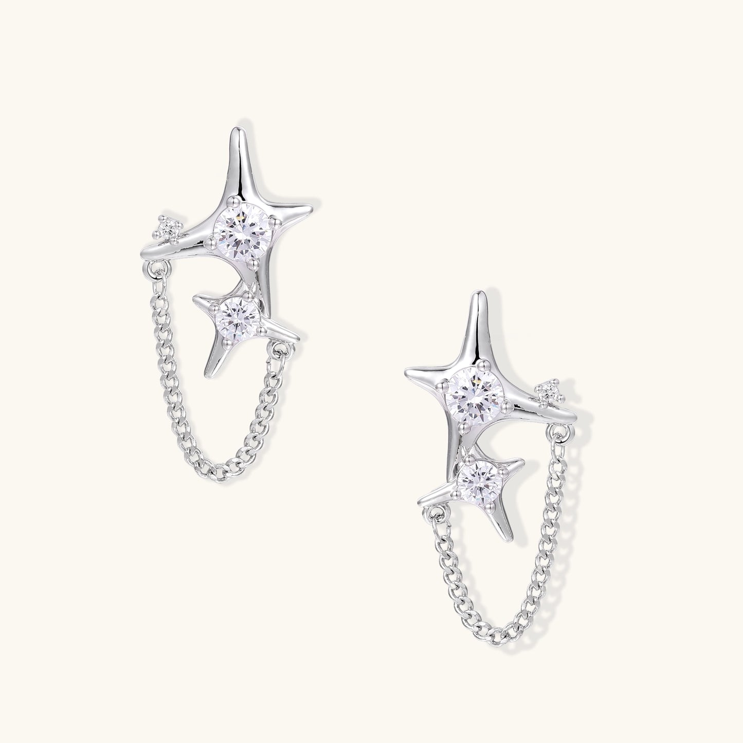 Delicate gold-plated star earrings with sparkling zirconia crystals connected by fine chains on cream background.