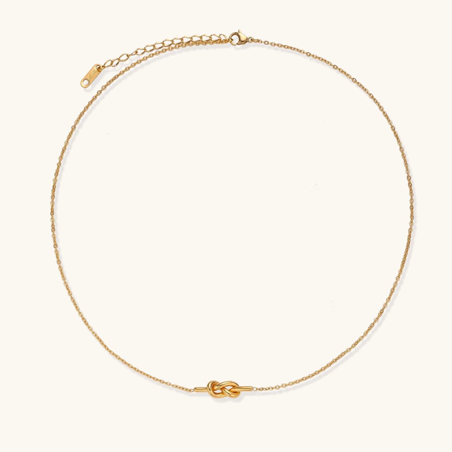 Dainty 18K gold plated stainless steel chain necklace with minimalist knot pendant on cream background.