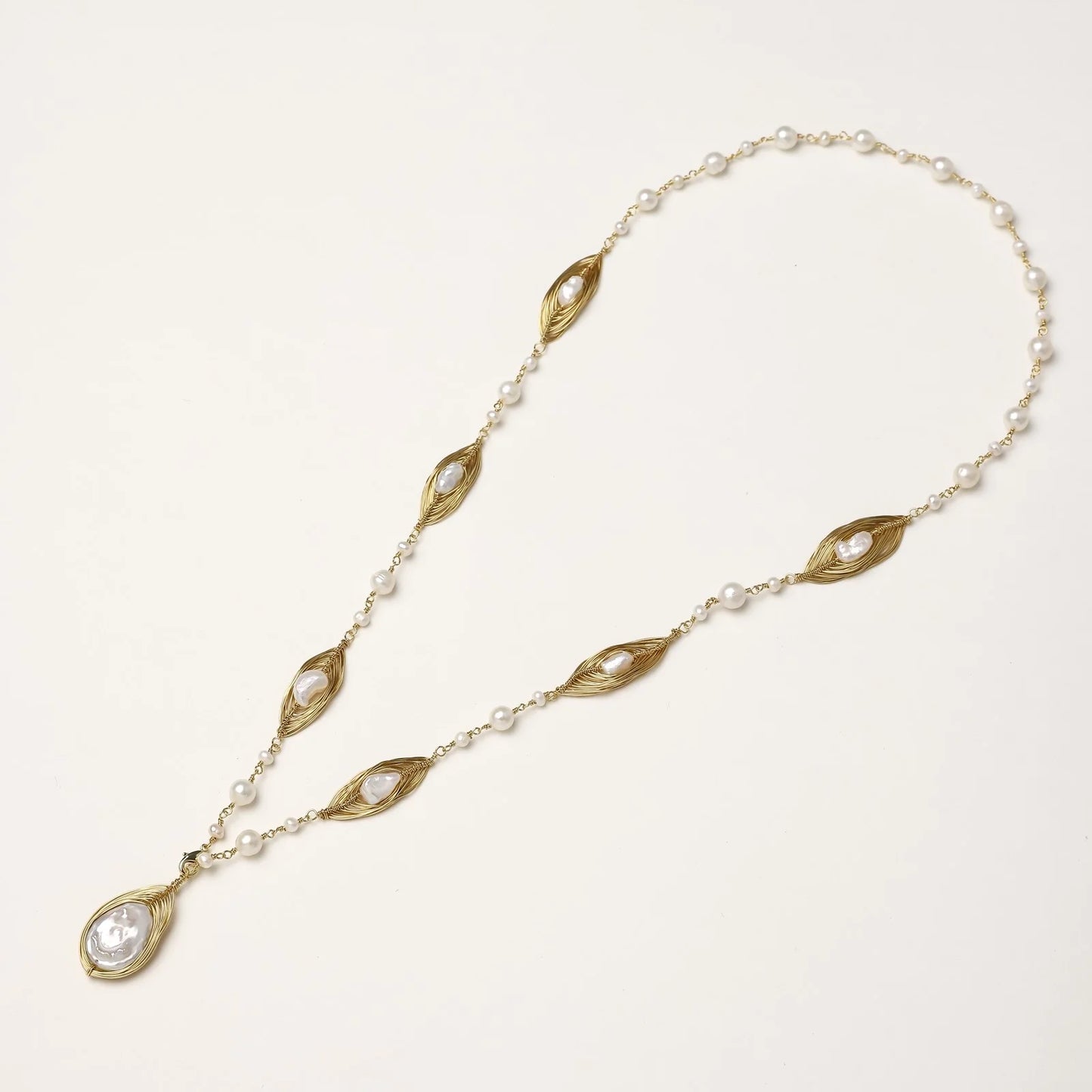 14K gold-plated necklace with eye-shaped stations and baroque pearl pendant on cream background