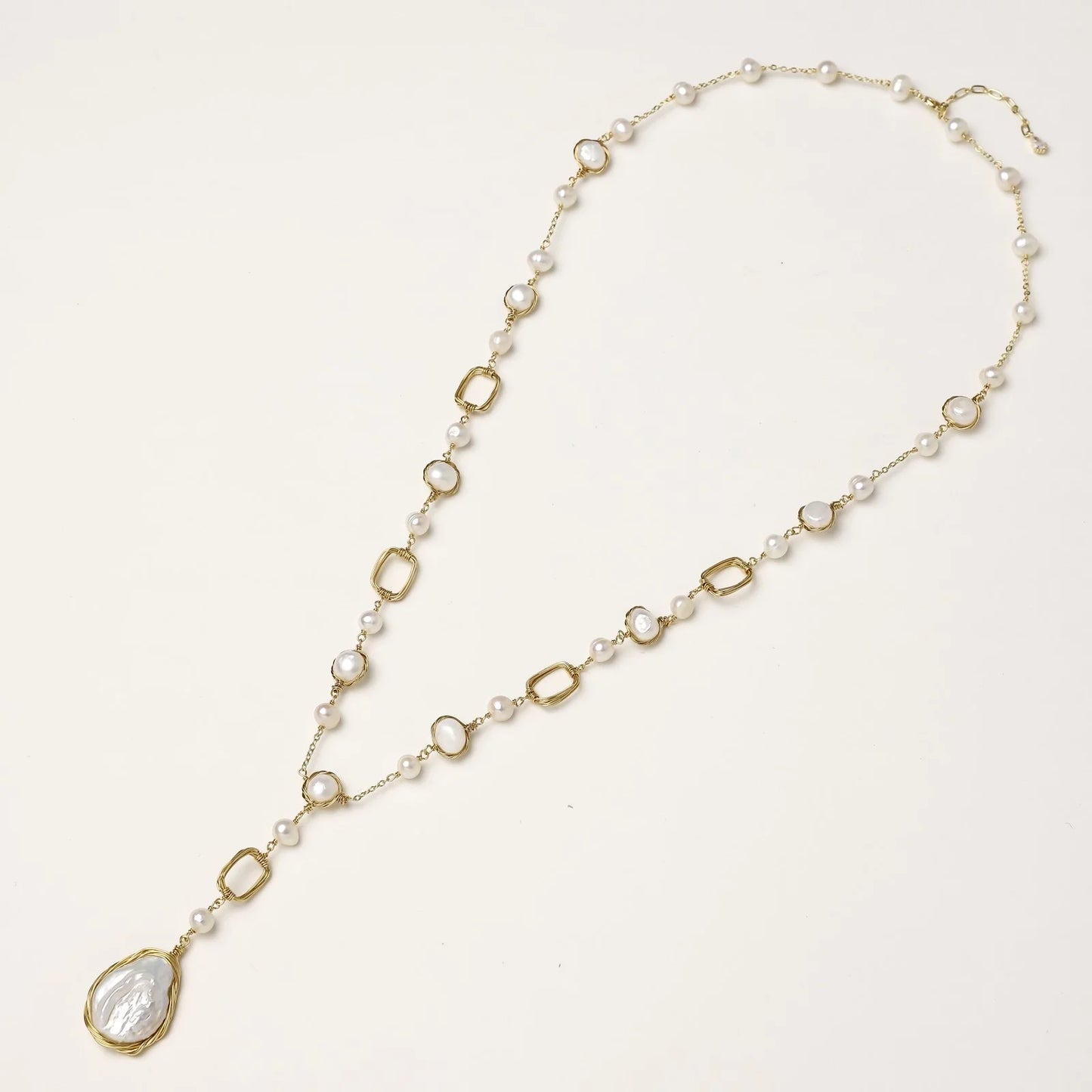 Y-shaped gold necklace with alternating geometric links, freshwater pearls, and baroque pearl pendant on cream background