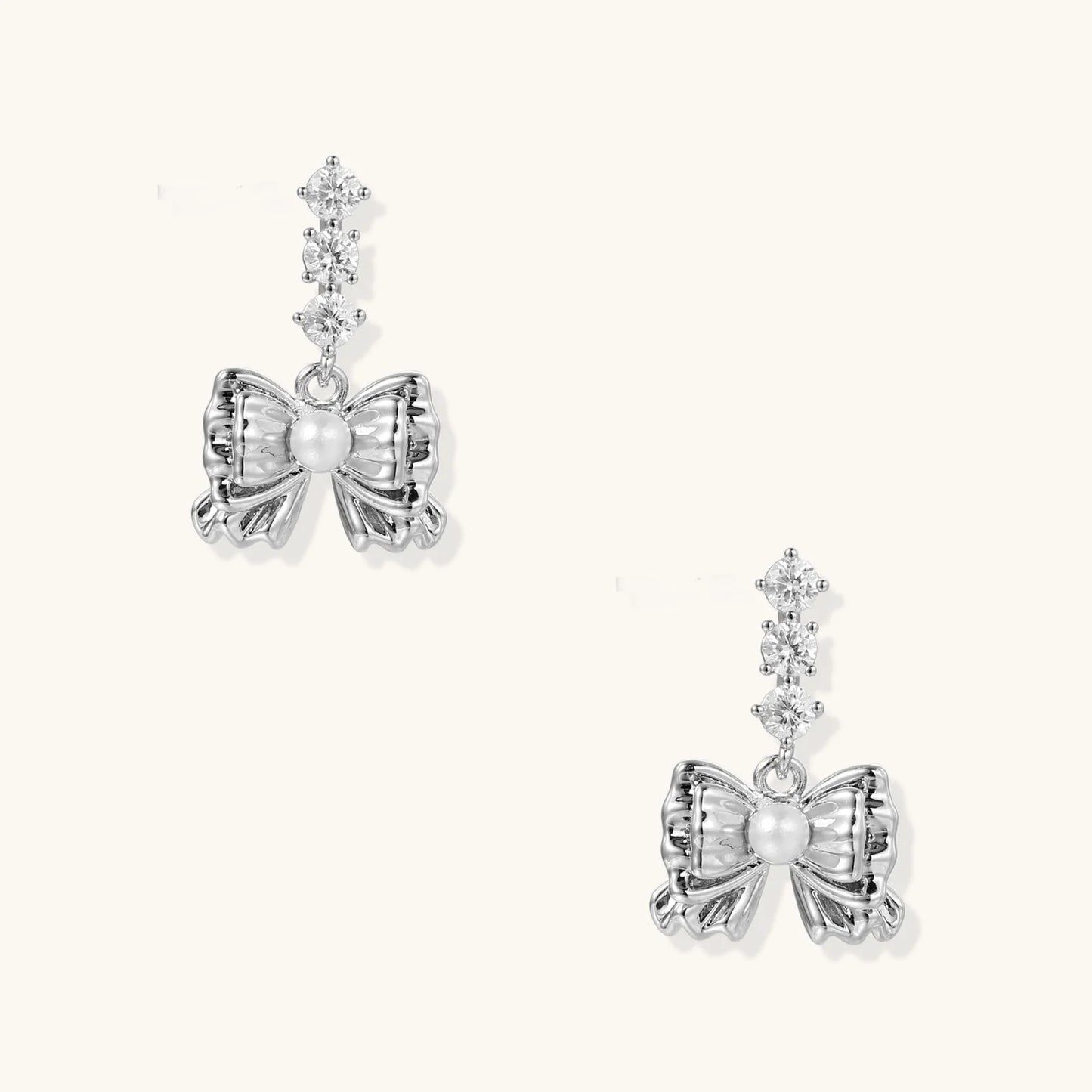 White gold plated drop earrings with three graduated zirconia crystals leading to a bow charm with pearl center