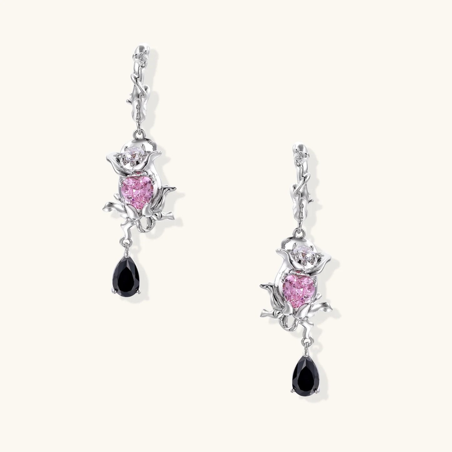 Silver-toned drop earrings with ornate rose design, pink zirconia center, and black teardrop stones on cream background
