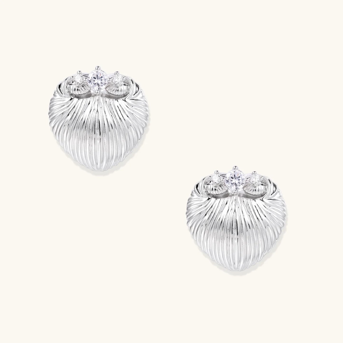 White gold-plated shell-textured stud earrings with three zirconia crystals on ridged surface against cream background.