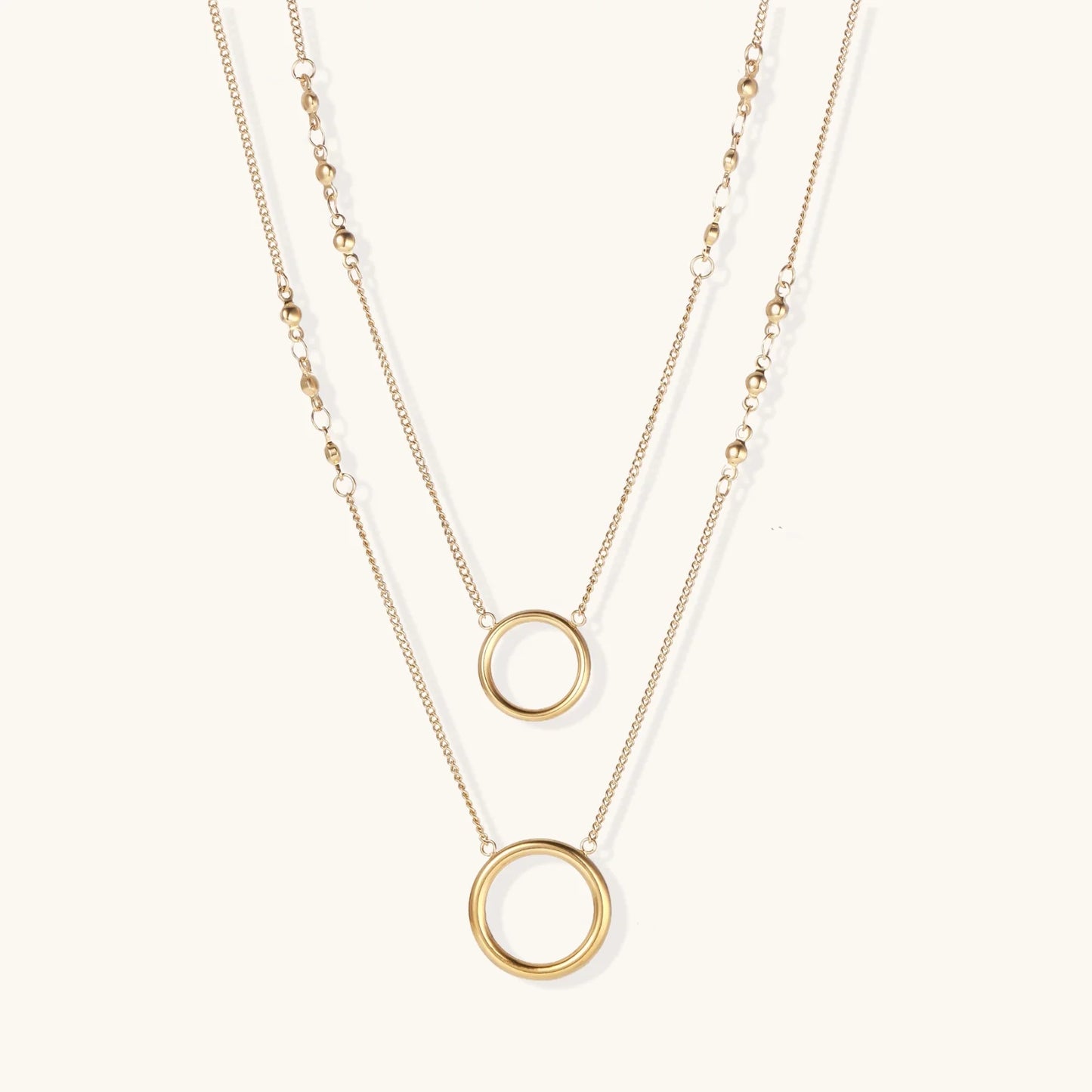 Layered gold necklace set with two open circle pendants and mixed chain styles on beige background