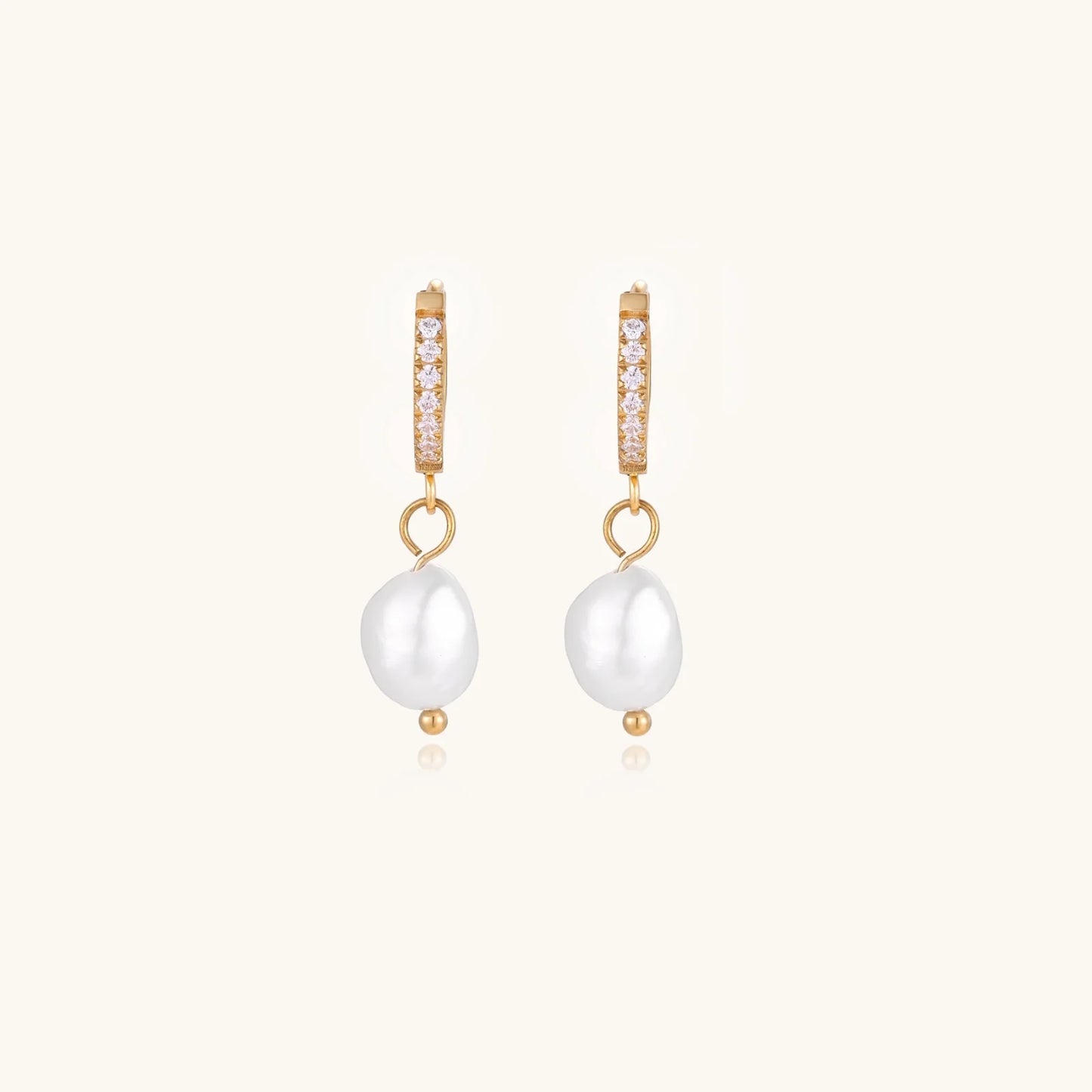 Gold huggie hoop earrings with pavé crystals and white freshwater pearl drops on cream background