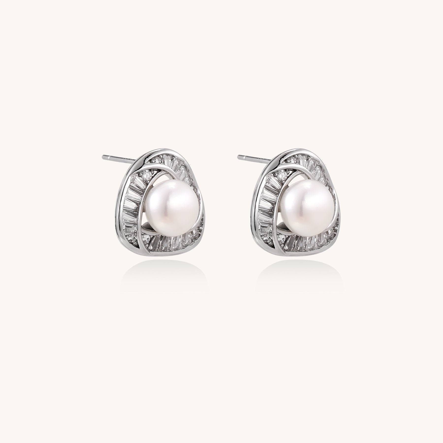 Close-up of triangular gold-plated stud earrings with central freshwater pearl surrounded by baguette crystals
