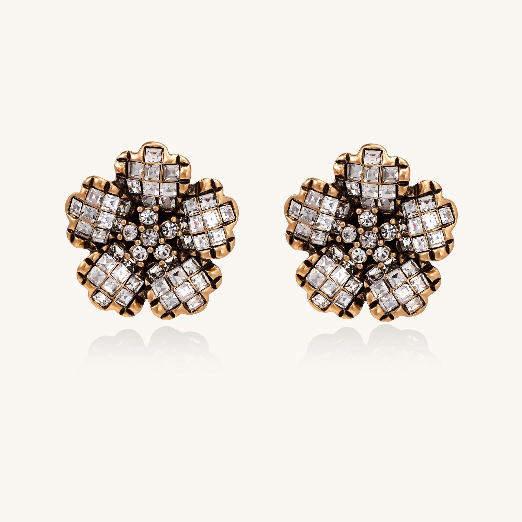 Ornate gold-plated flower earrings with clear zirconia crystals arranged in dimensional petal formations on cream background.