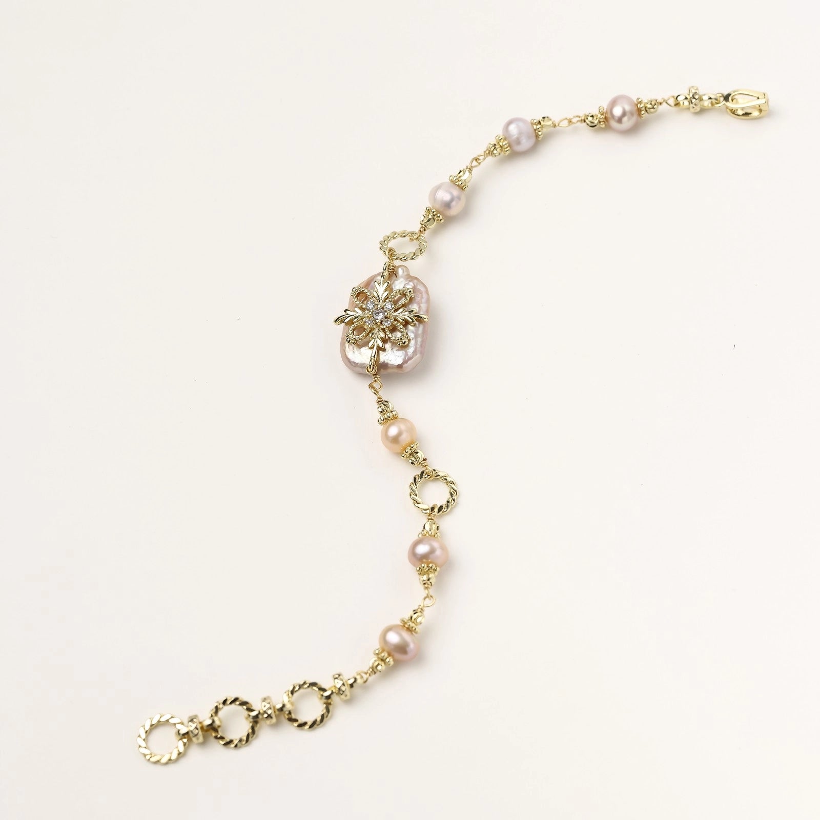 Gold-plated chain bracelet with baroque pearl centerpiece and floral charm, featuring mixed freshwater pearls.
