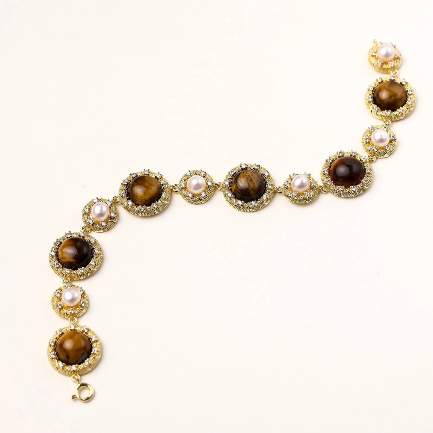 Ornate gold-plated bracelet with alternating brown tiger's eye stones and white freshwater pearls in crystal-accented settings