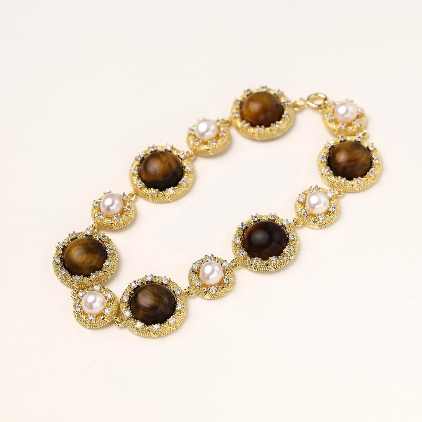 Ornate gold-plated bracelet with alternating brown tiger's eye stones and white freshwater pearls in crystal-accented settings