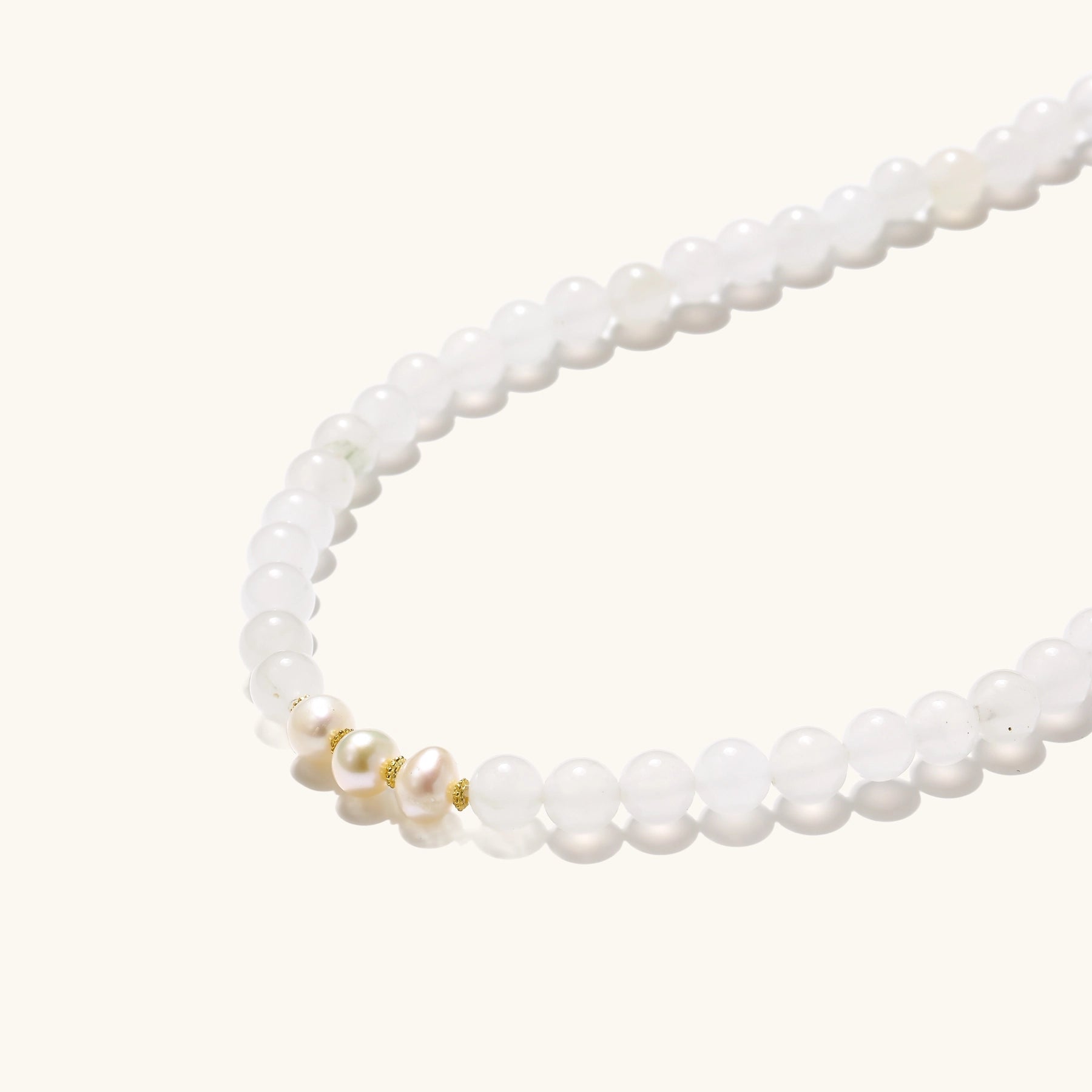 Stretch bracelet with white jade beads, freshwater pearls, and orange agate centerpiece on cream background.