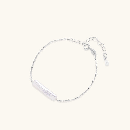 Delicate sterling silver chain bracelet with an organic white baroque pearl centerpiece on neutral background