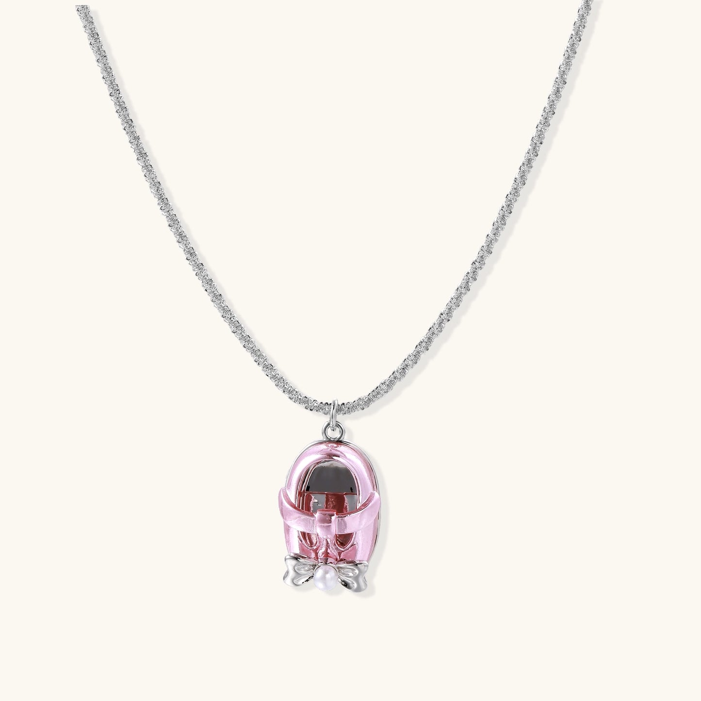 Delicate gold-plated chain necklace with transparent pink-tinted capsule pendant containing decorative bow element