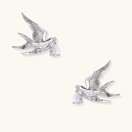 Gold-plated brass swallow earrings with detailed wing engravings carrying clear zirconia crystal drops in their beaks