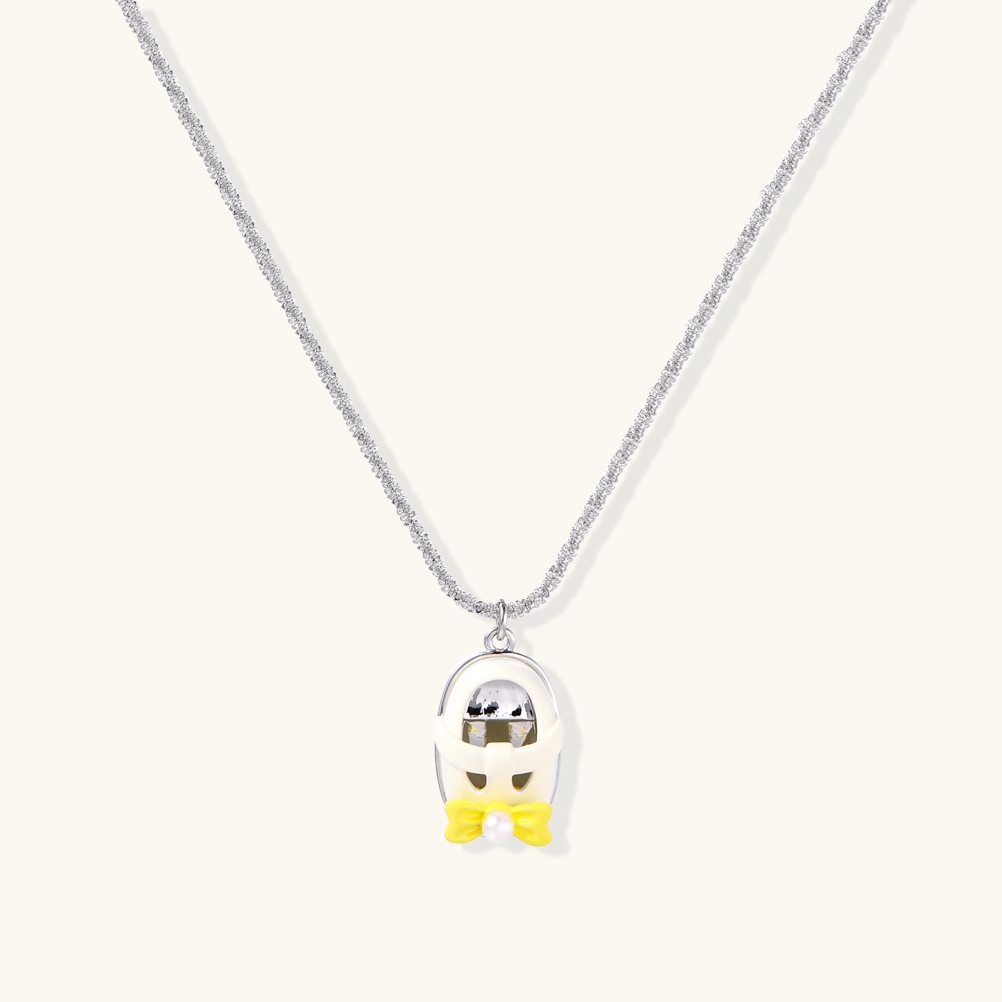 Minimalist gold plated brass necklace with cute capsule pendant featuring yellow bow detail on neutral background.