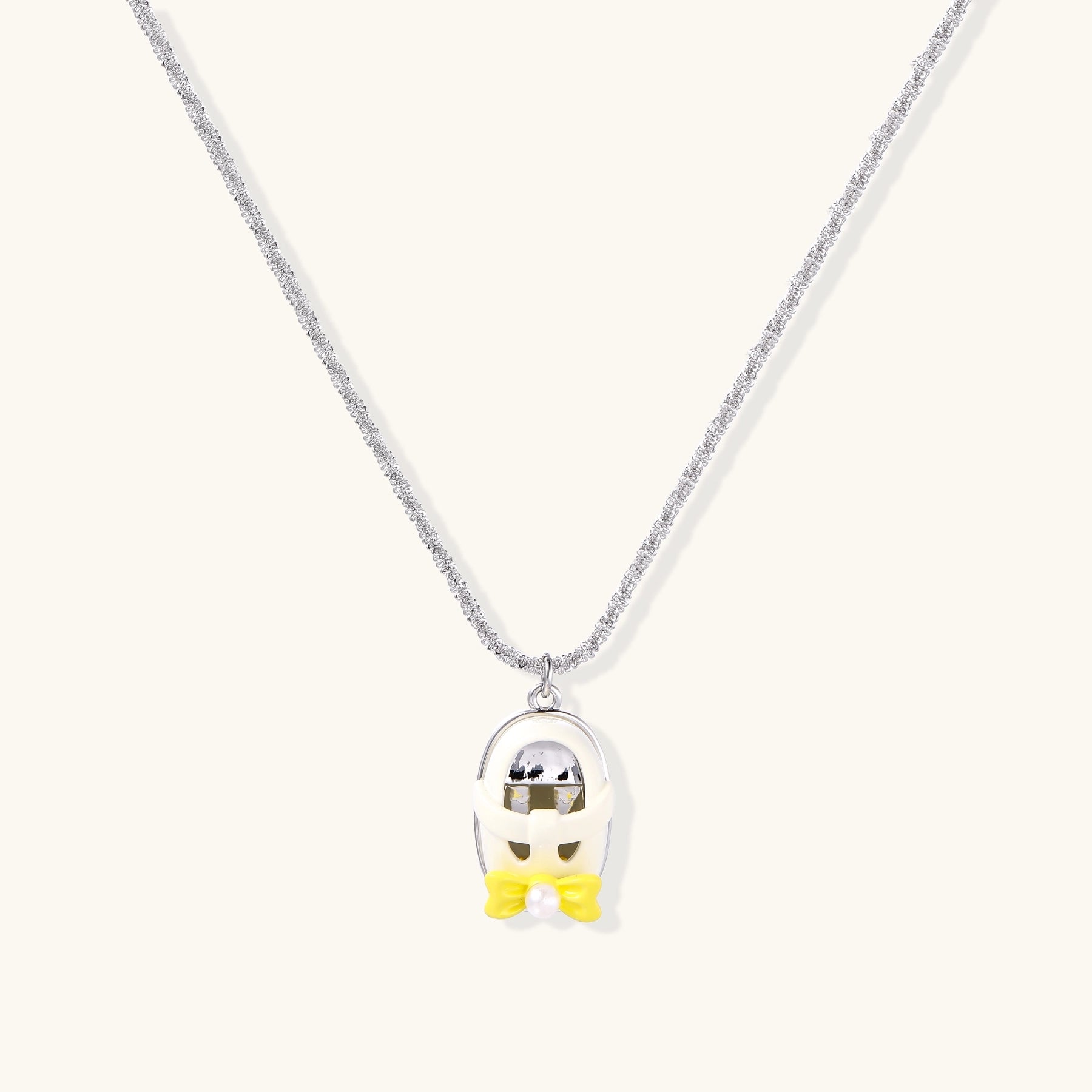 Minimalist gold plated brass necklace with cute capsule pendant featuring yellow bow detail on neutral background.