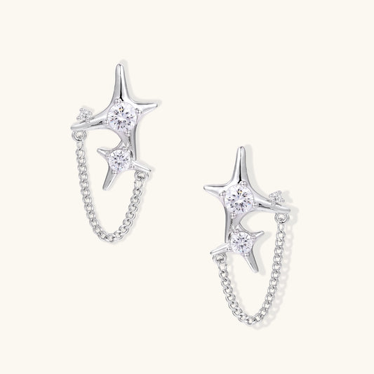 Delicate gold-plated star earrings with sparkling zirconia crystals connected by fine chains on cream background.