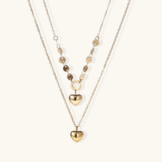 Three-layer gold-plated necklace set with disc chain and two heart pendants on neutral background
