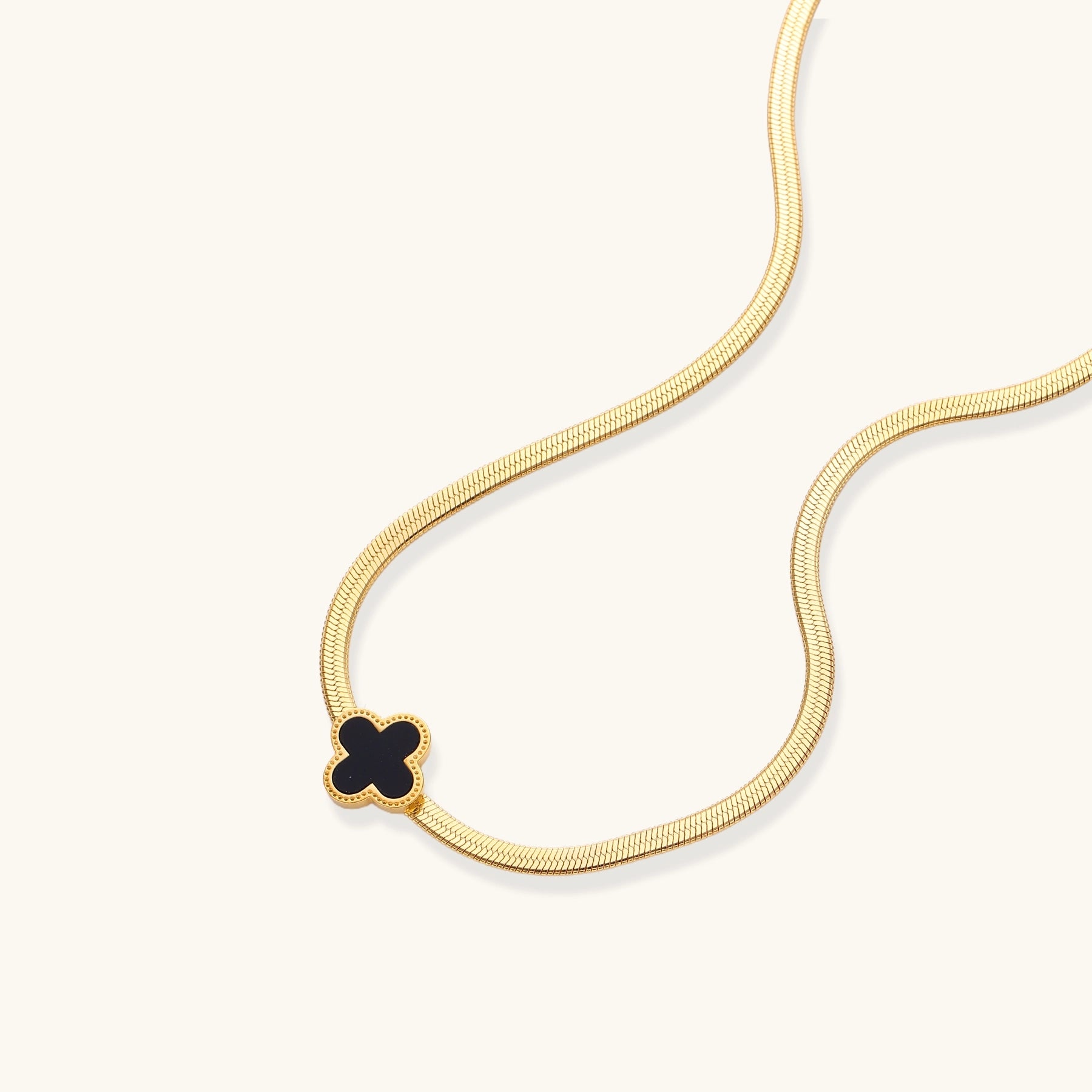 Delicate gold-plated chain necklace featuring a black quatrefoil clover pendant on white background.