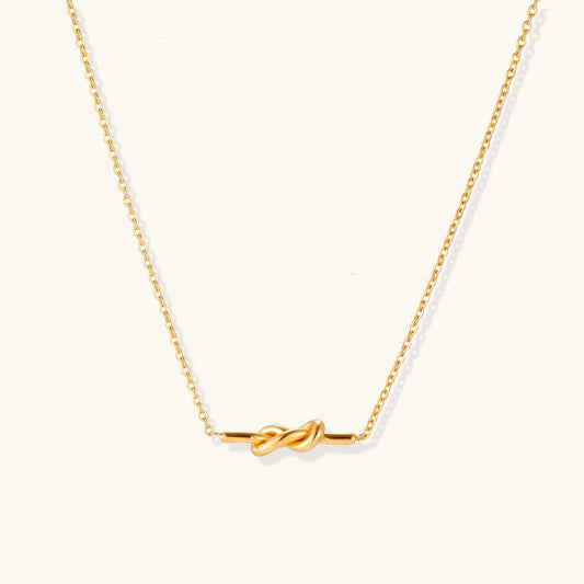 Dainty 18K gold plated stainless steel chain necklace with minimalist knot pendant on cream background.