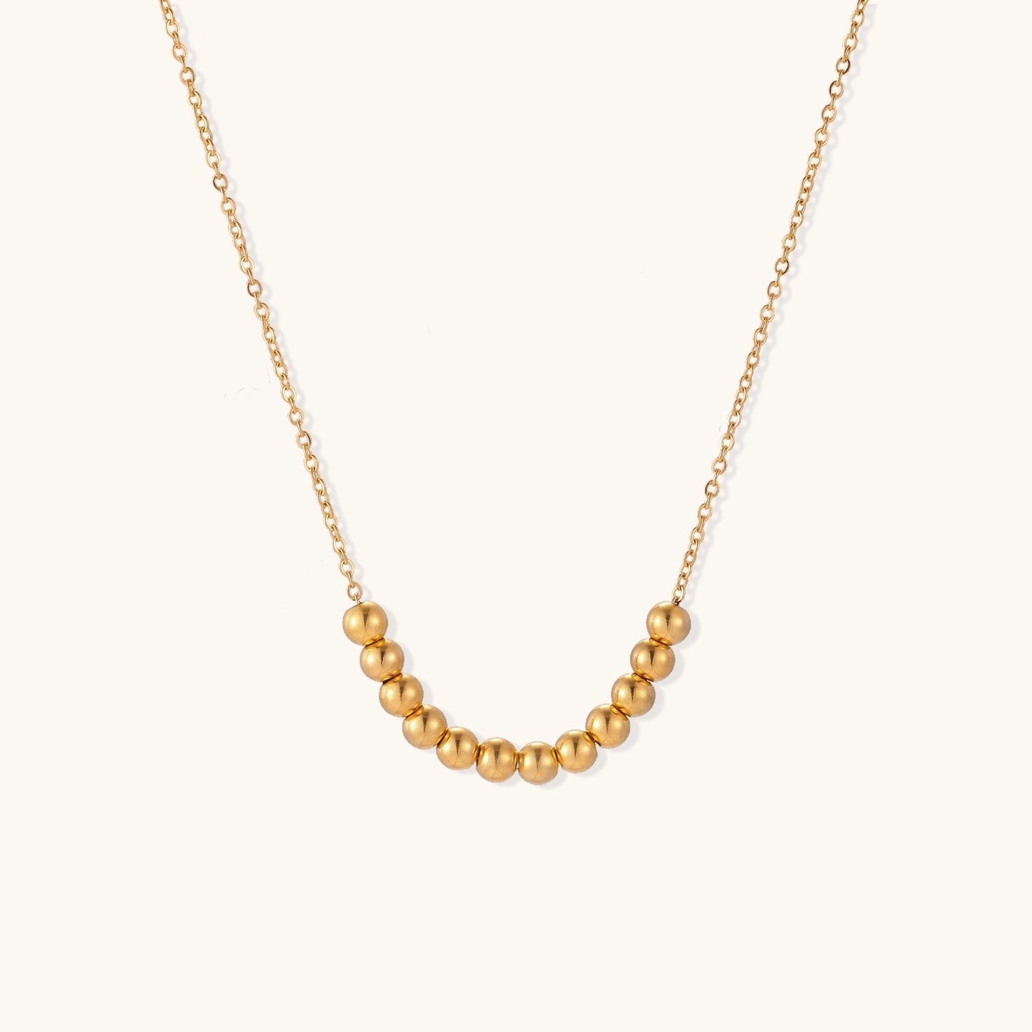 Delicate gold-plated chain necklace featuring clustered spherical beads arranged in elegant curve against white background.