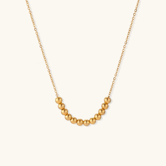 Delicate gold-plated chain necklace featuring clustered spherical beads arranged in elegant curve against white background.