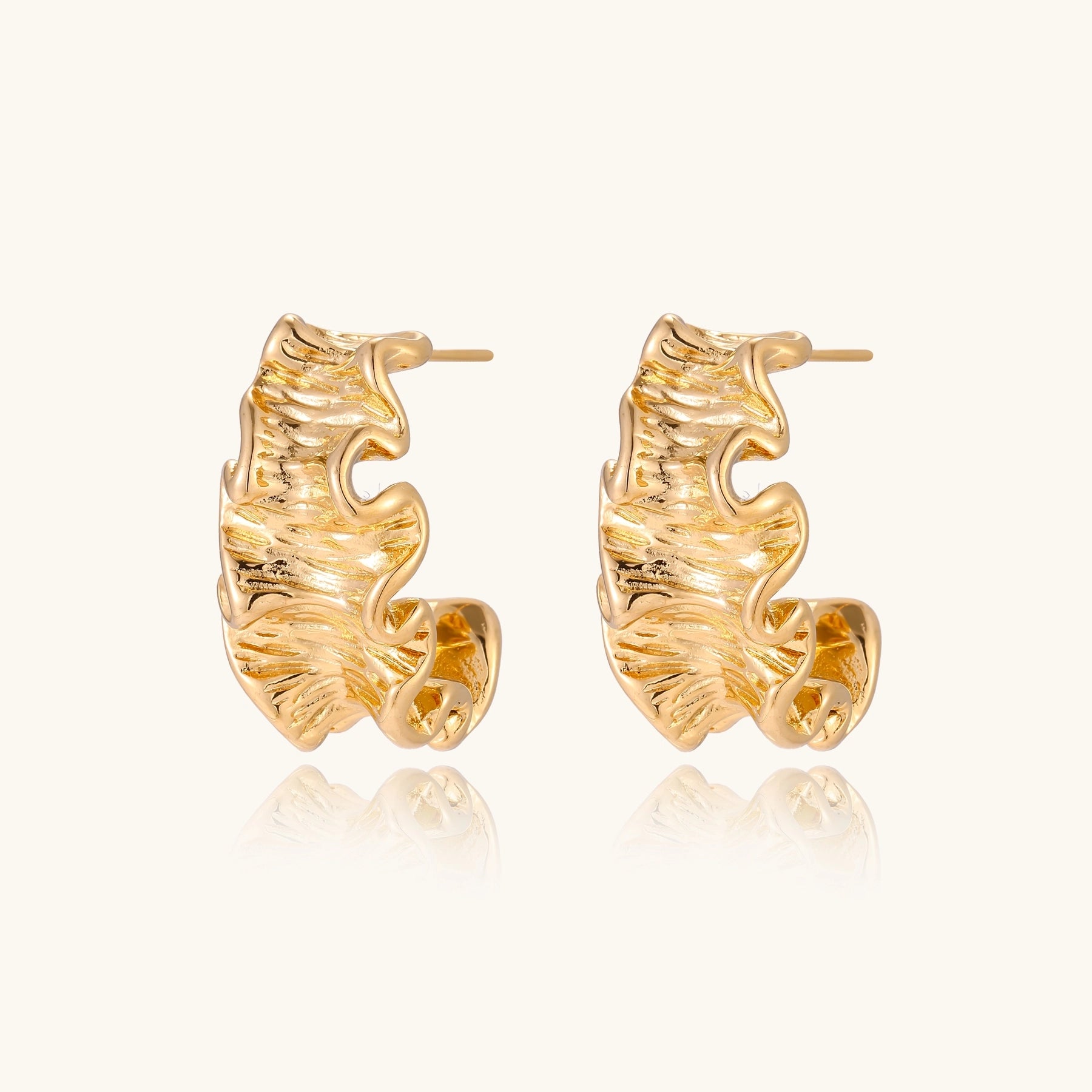 Close-up of dimensional gold-plated hoop earrings with rippled wave texture against white background.