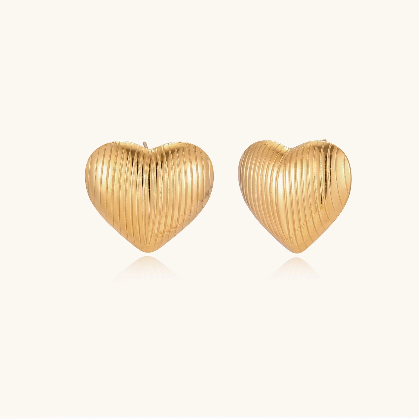 Close-up of ridged heart-shaped gold-plated stud earrings with textured surface pattern on cream background.