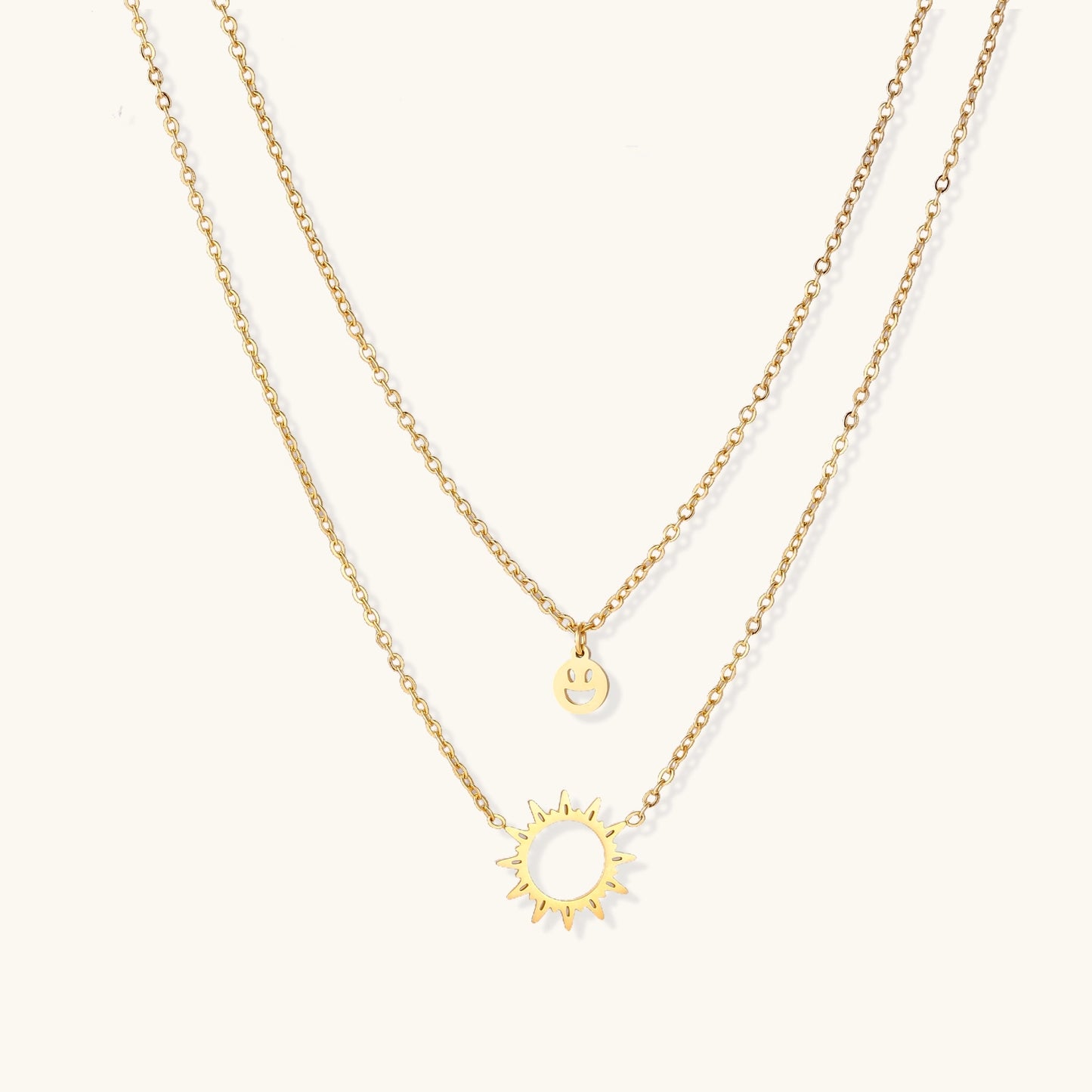 Delicate gold-plated layered necklace with smiley face and sun pendants on white background, showing adjustable chain.