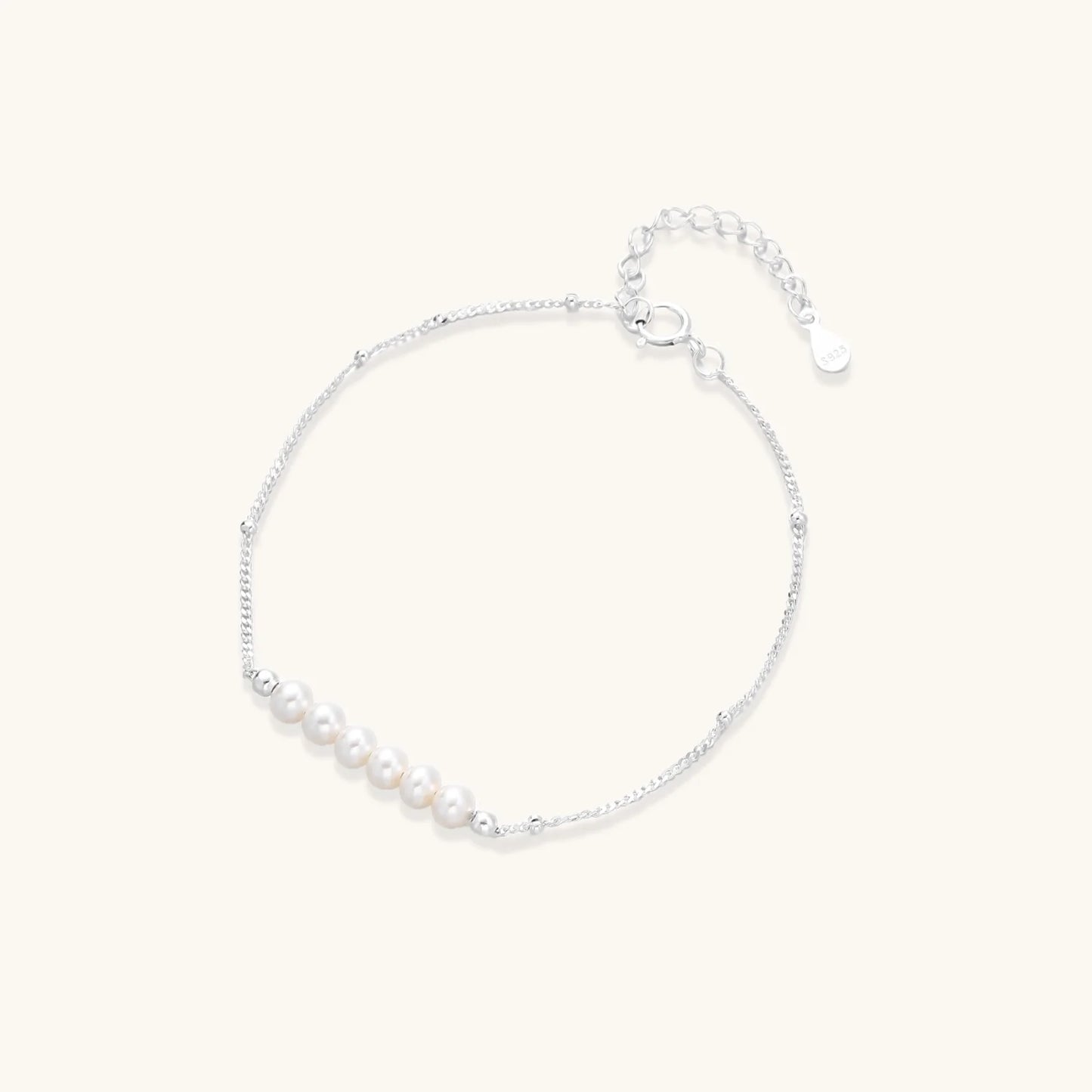 Delicate rhodium-plated silver chain bracelet with row of small baroque pearls centered on white background.