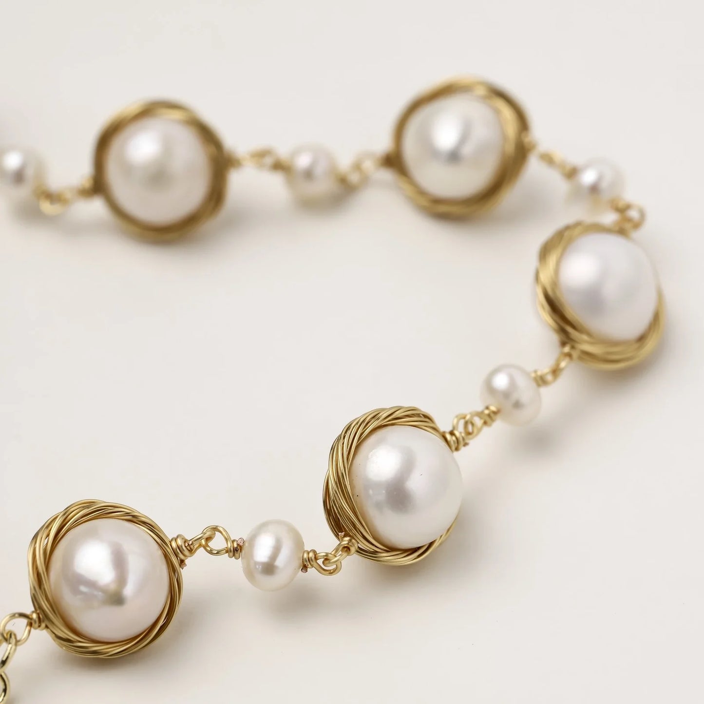 Gold wire-wrapped freshwater pearl bracelet with alternating pearl sizes on cream background, adjustable length