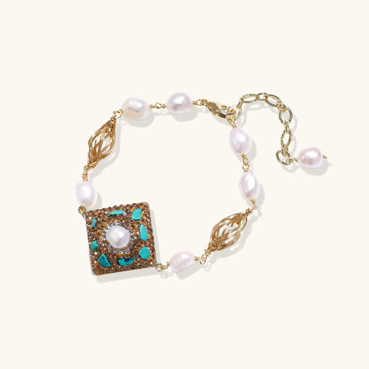 Gold-plated bracelet with baroque centerpiece, turquoise stones, freshwater pearls, and ornate chain links on cream background.