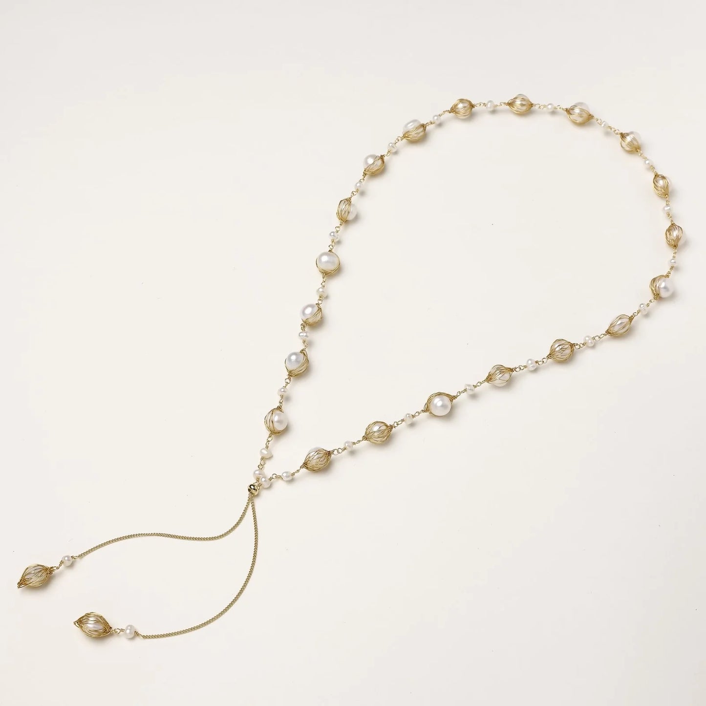 Adjustable gold lariat necklace with freshwater pearls nested in delicate cage settings and Y-shaped tassel drop