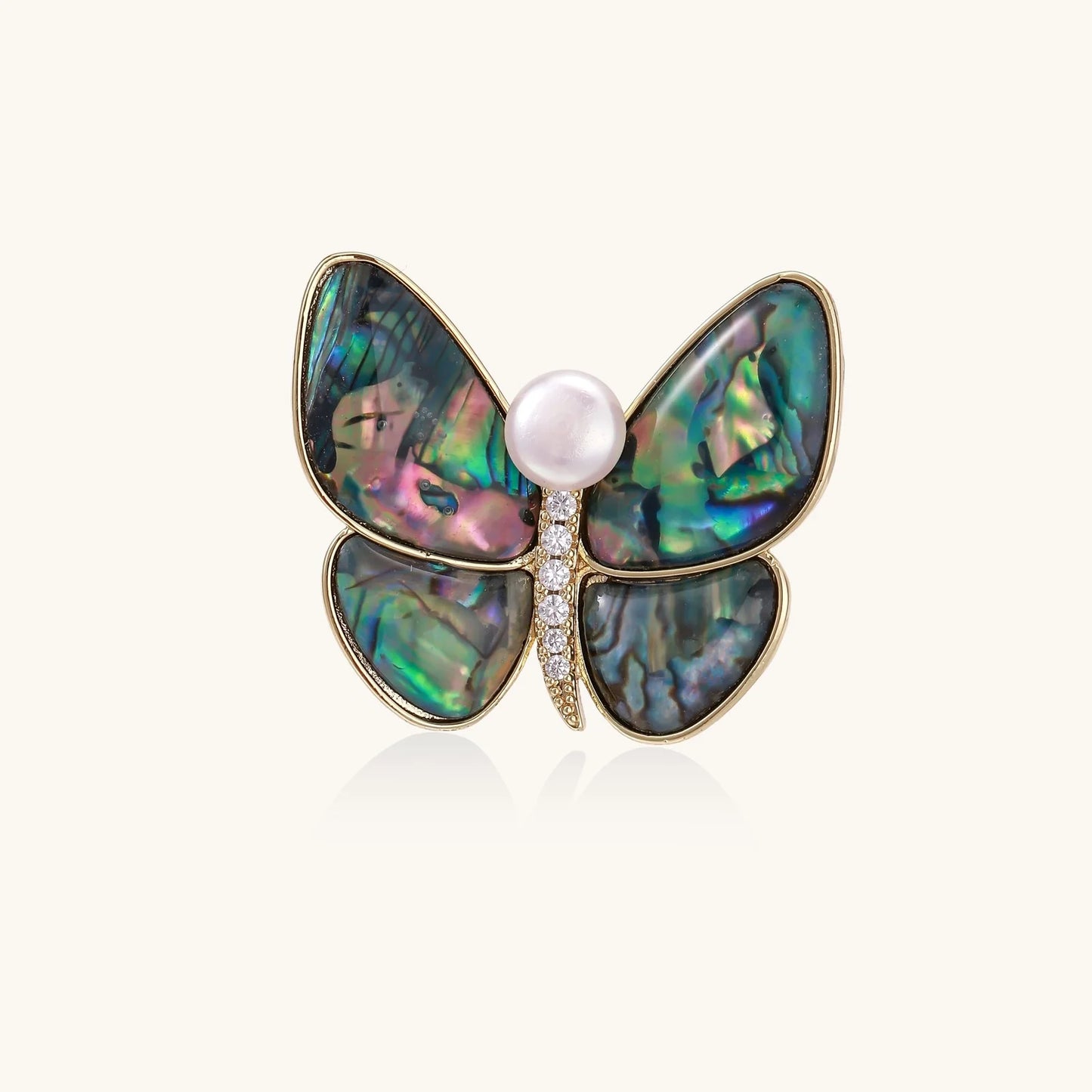 Gold-plated butterfly brooch with iridescent abalone shell wings and freshwater pearl accent on cream background.