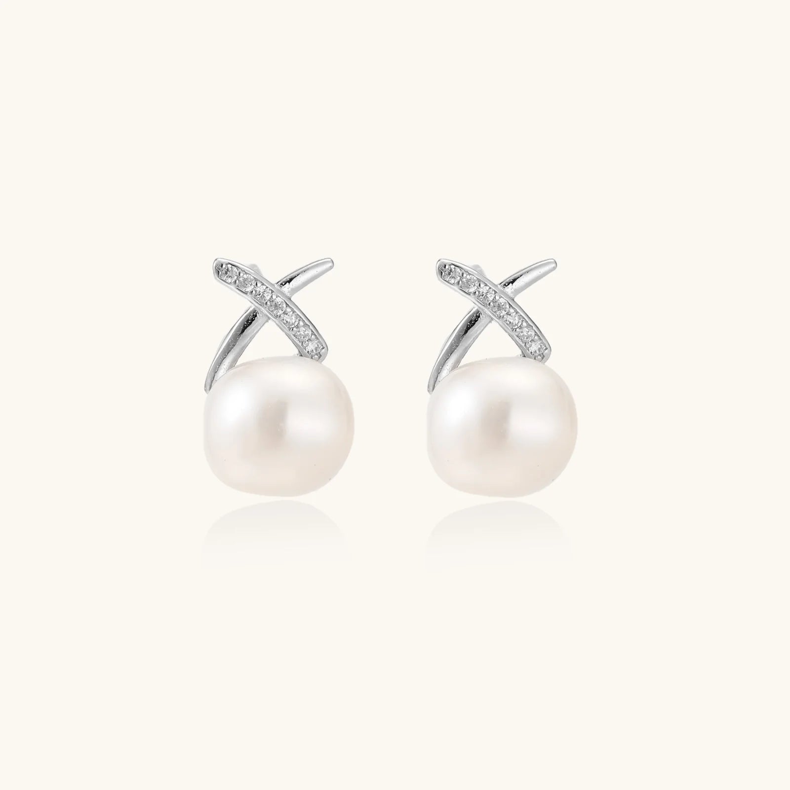 Rhodium-plated silver stud earrings with sparkling X design above lustrous round freshwater pearls on white background.