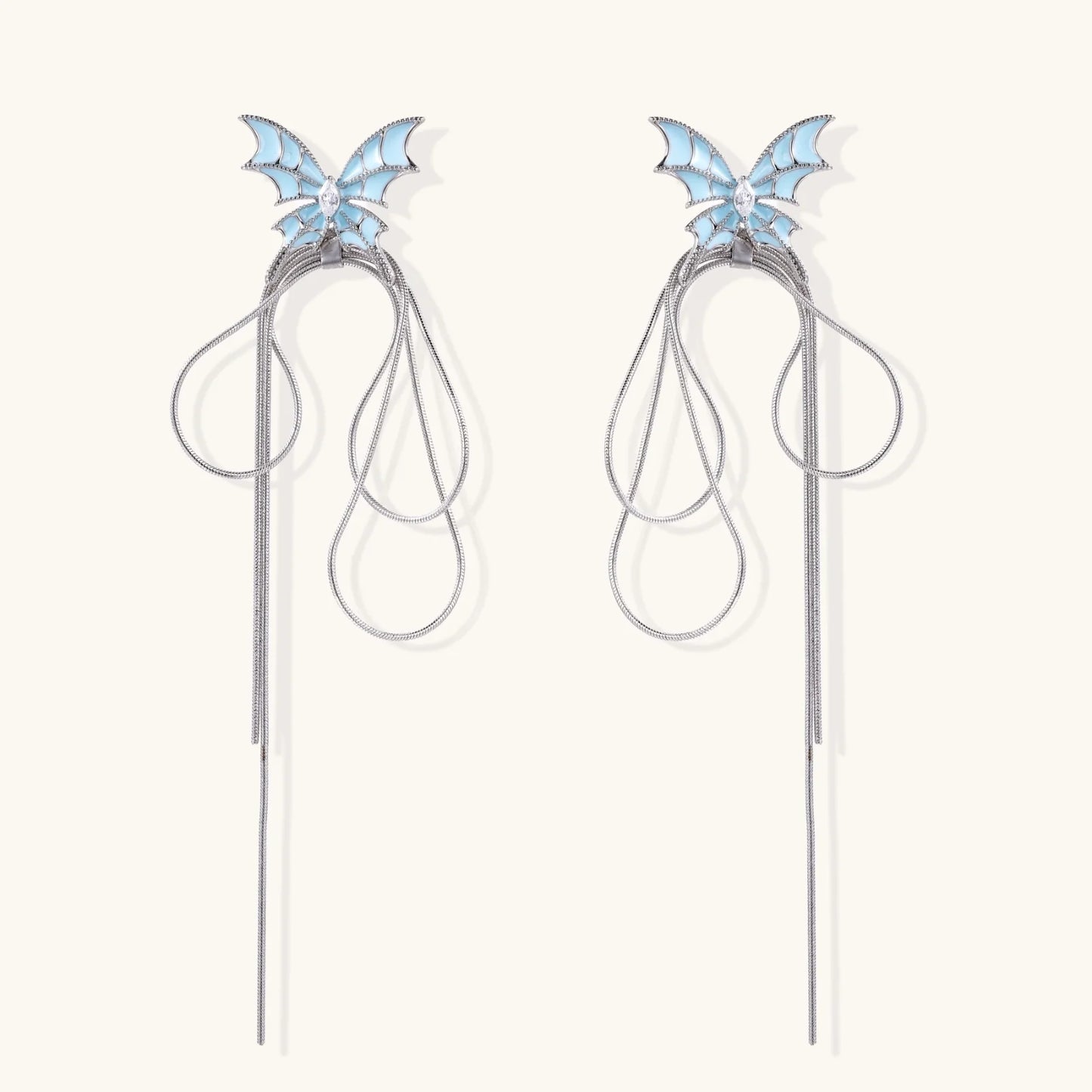 Long silver-tone earrings with powder blue enamel butterfly studs and flowing chain tassels on cream background