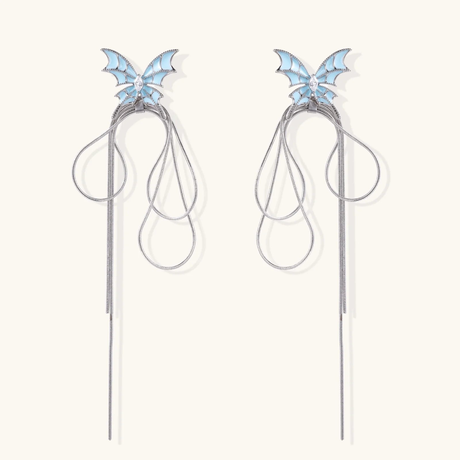 Long silver-tone earrings with powder blue enamel butterfly studs and flowing chain tassels on cream background