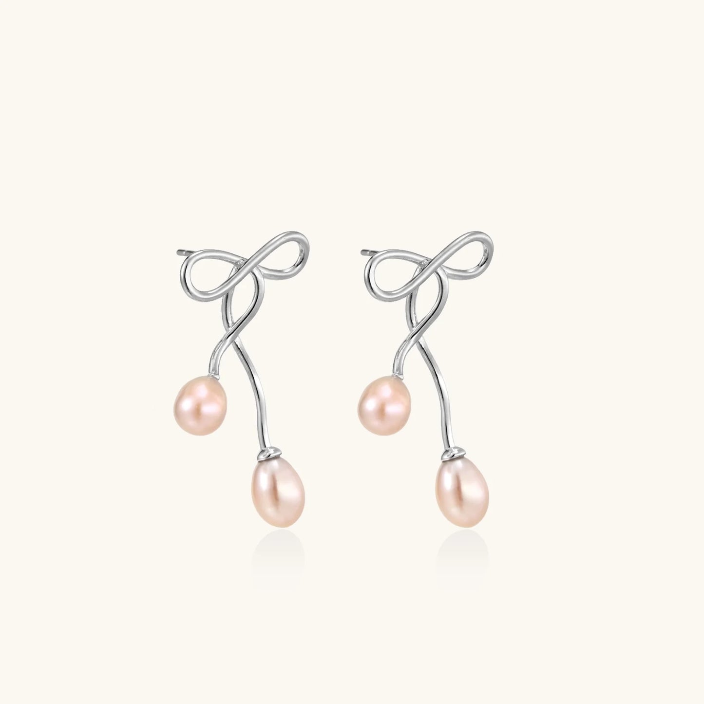 Rhodium-plated silver earrings with organic vine curves and two peachy freshwater pearls on cream background