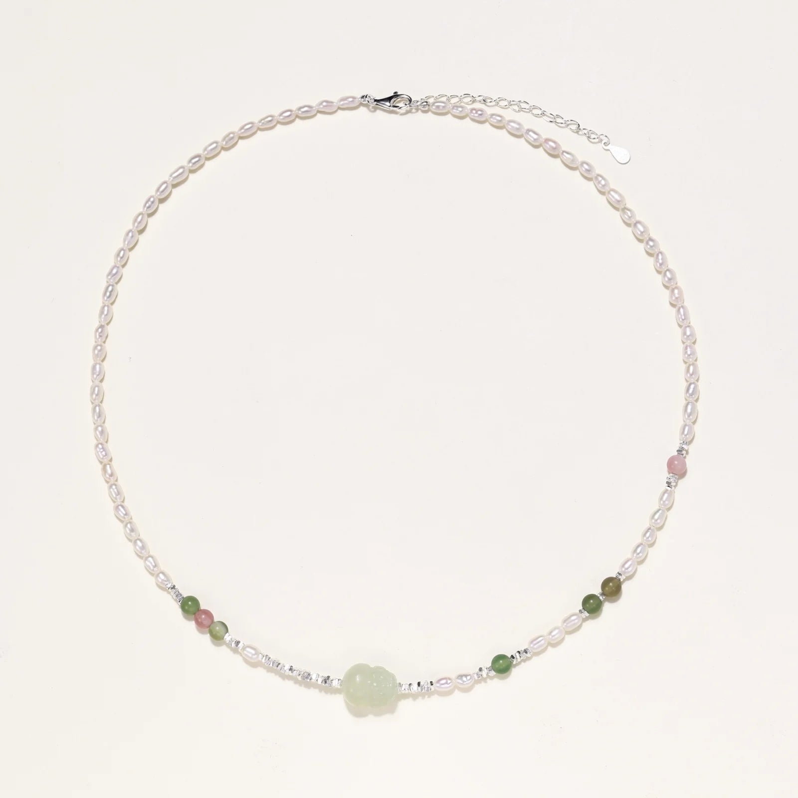 Delicate pearl necklace with pale green serpentine jade centerpiece and colorful agate beads on cream background