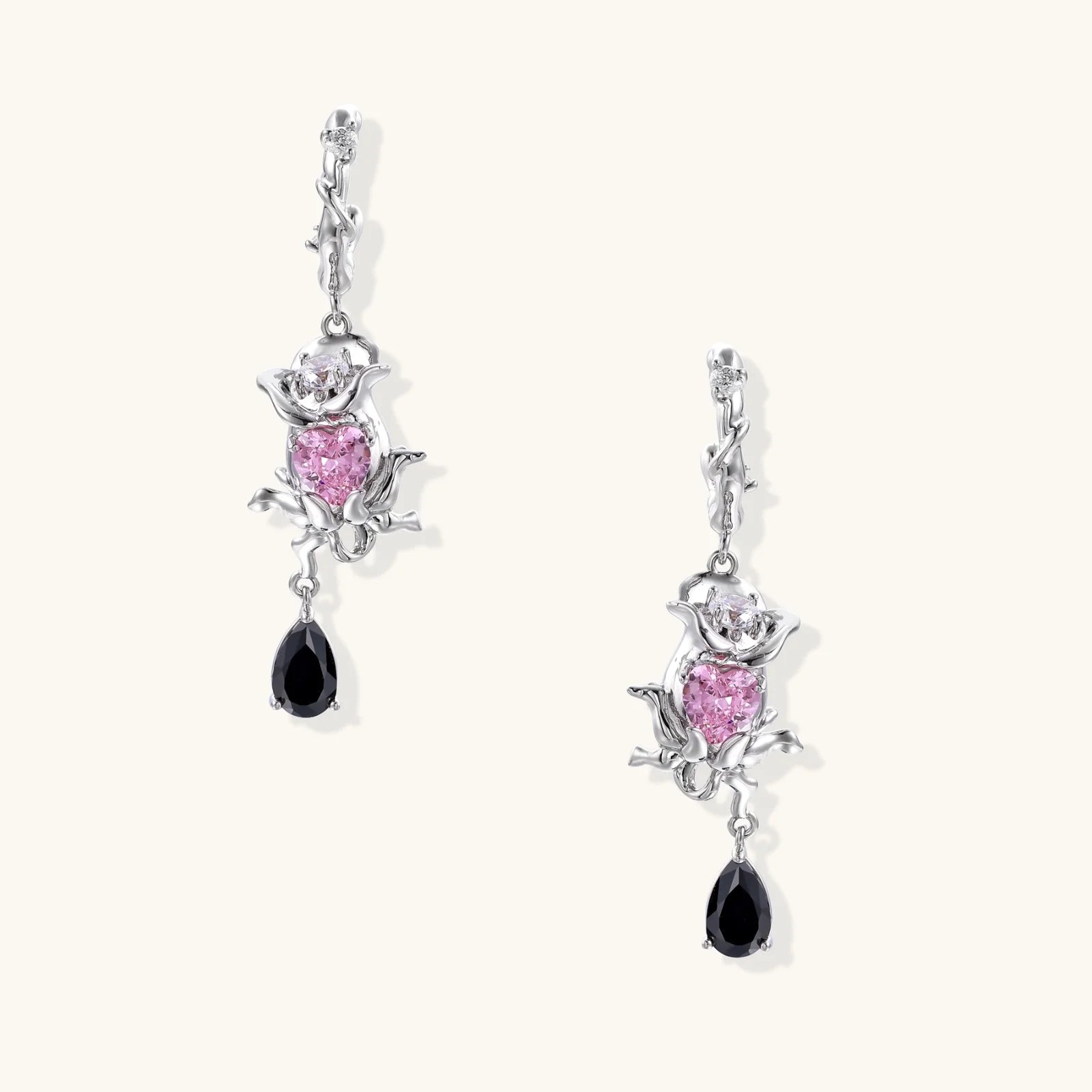 Silver-toned drop earrings with ornate rose design, pink zirconia center, and black teardrop stones on cream background