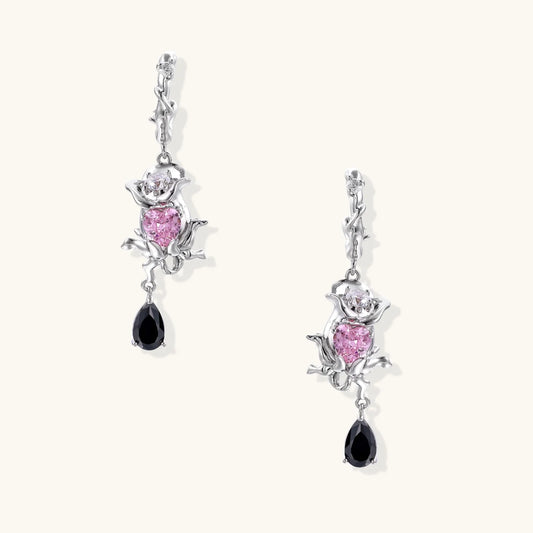 Silver-toned drop earrings with ornate rose design, pink zirconia center, and black teardrop stones on cream background