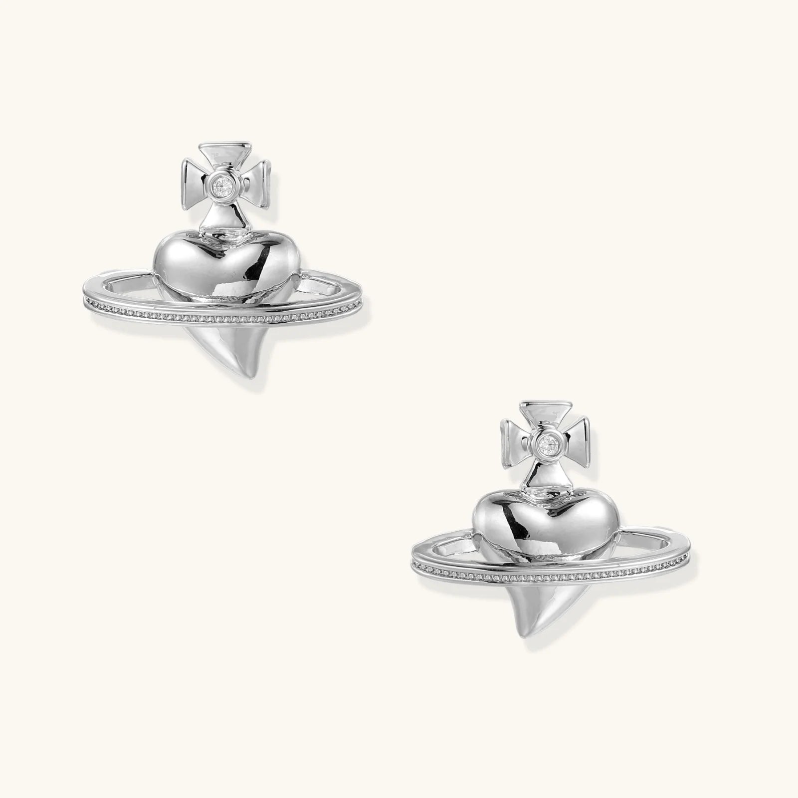 Polished white gold-plated Saturn planet stud earrings with orbital rings and crystal-centered cross on beige background