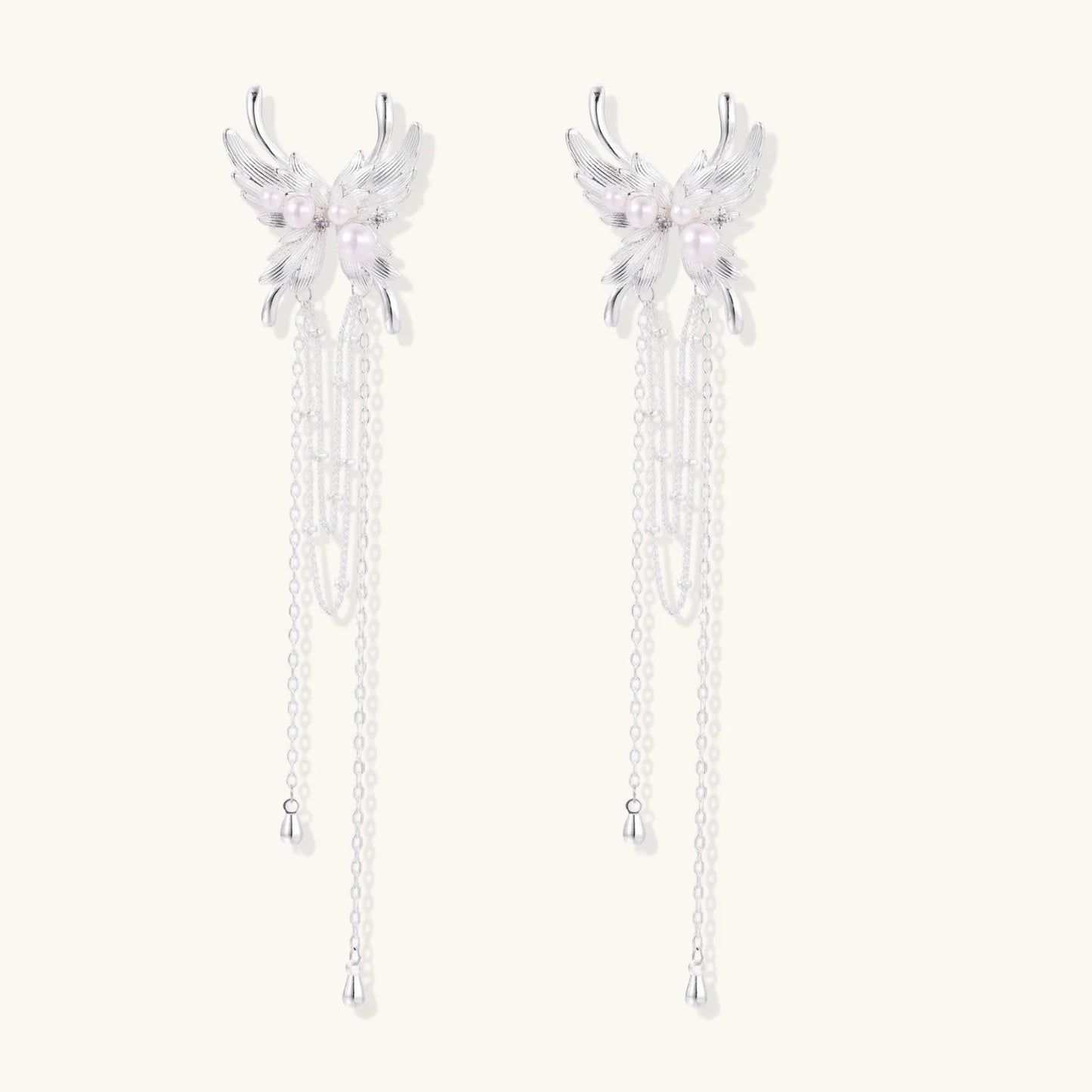 Elegant chandelier earrings with phoenix wing design, white pearls, and cascading silver chains on cream background