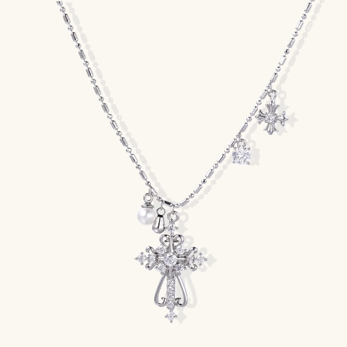 Ornate white gold-plated cross pendant with zirconia stones and pearl accents on adjustable silver chain against cream background