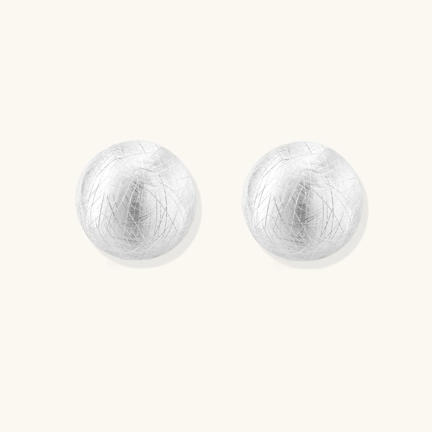Brushed sterling silver half-dome clip-on earrings with textured surface against cream background