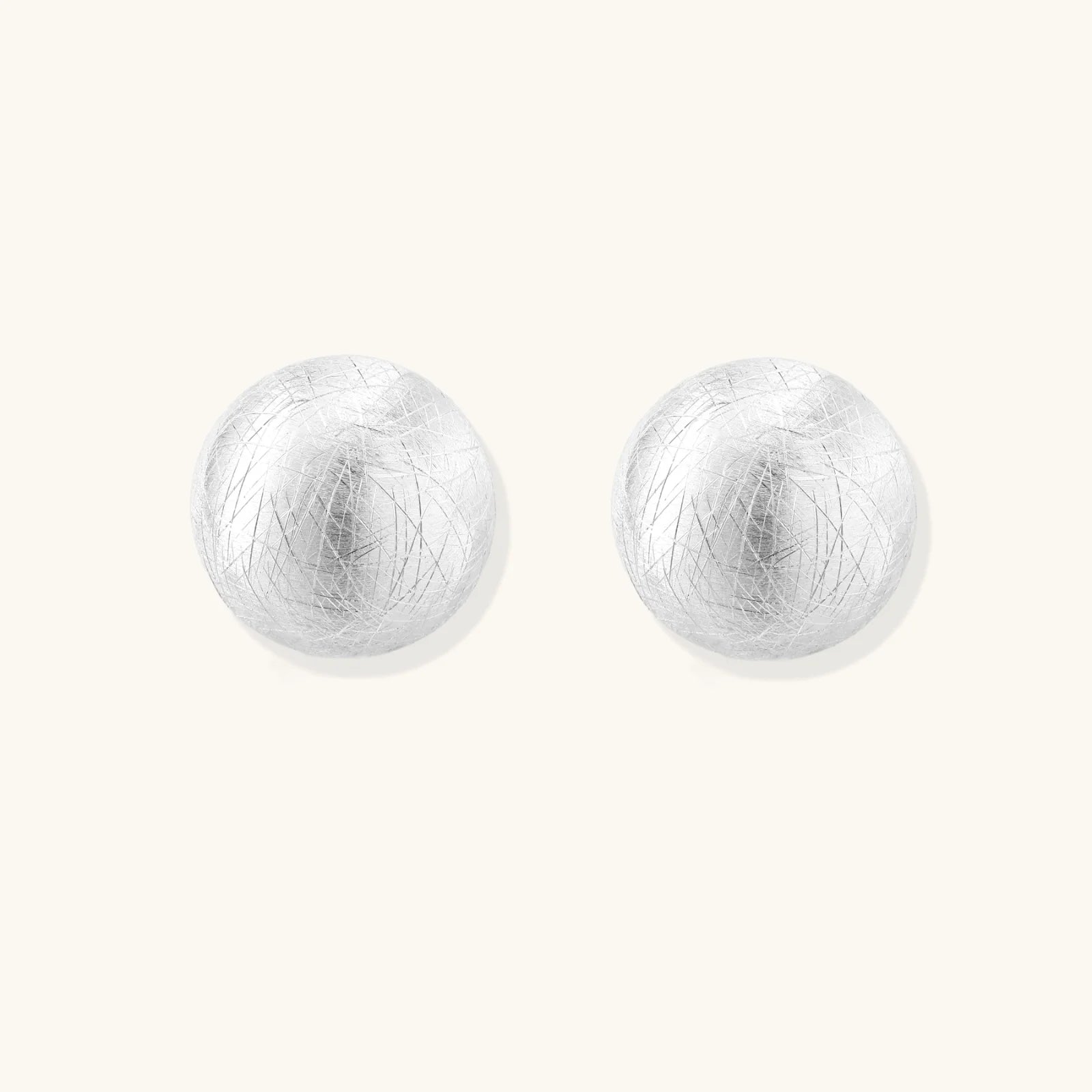 Brushed sterling silver half-dome clip-on earrings with textured surface against cream background
