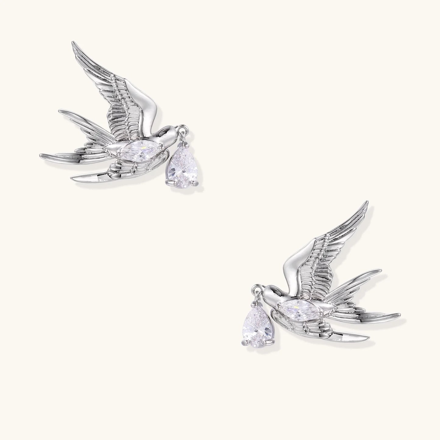 Silver-toned swallow stud earrings with detailed wings carrying teardrop zirconia crystals on white background